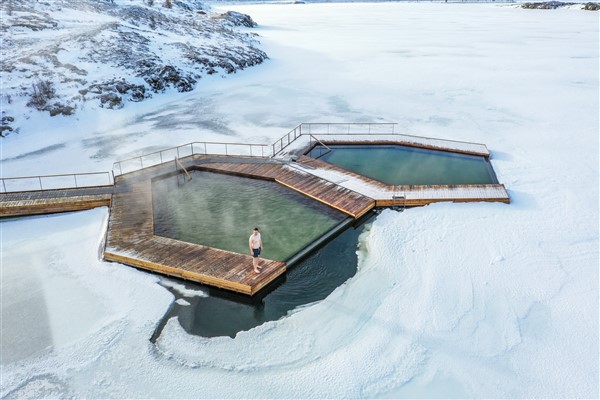 Een man staat naast een warmwaterbron in een meer met rondom bevroren water en sneeuw op het land