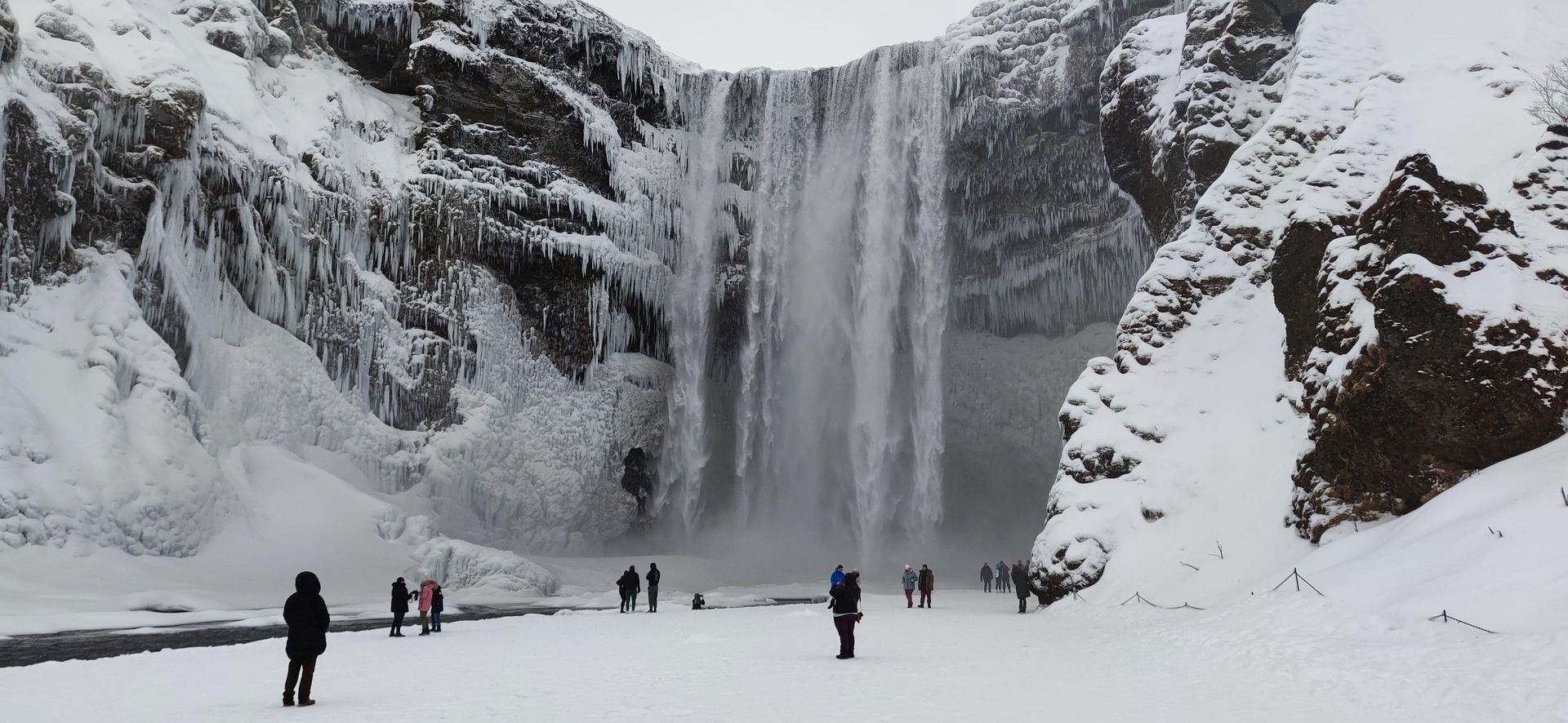 Een bevroren waterval met besneeuwde voorgrond en kijkende mensen