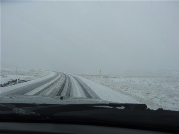 Een besneeuwde weg en omgeving gezien vanuit de auto