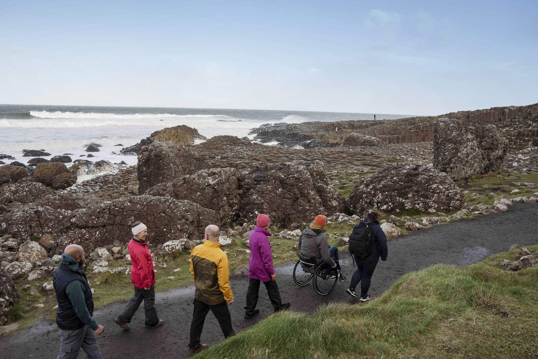 Een groepje wandelaars loopt langs de kust in Ierland, in het gezelschap van een rolstoeler