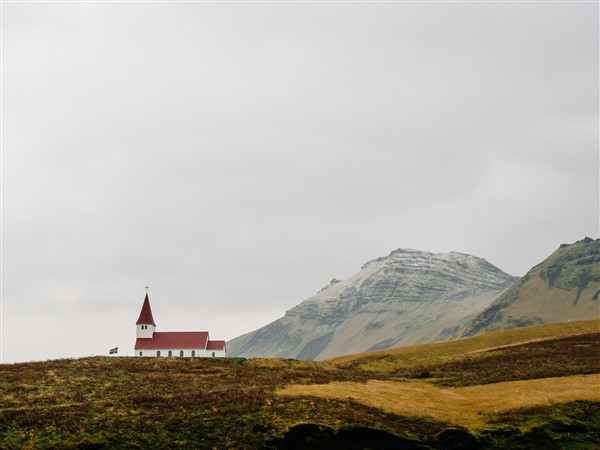 a white building with a red roof on a hill with mountains in the background