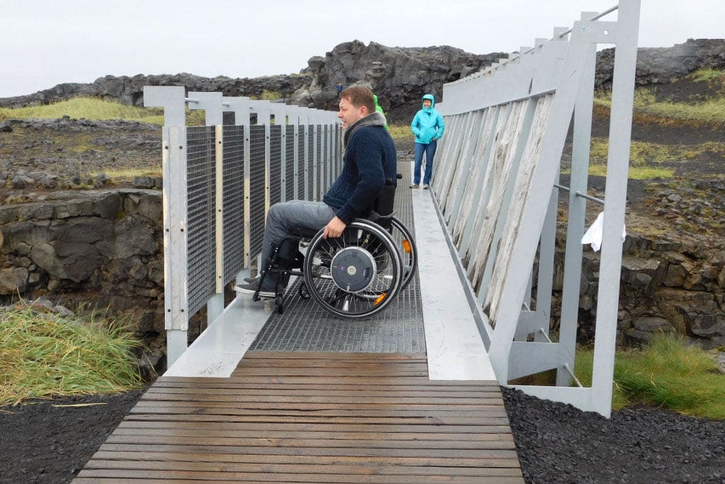 Een man in een rolstoel op een brug tussen 2 continenten op IJsland