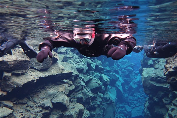 Snorkelaar in de kristalheldere wateren van de Silfra-kloof in IJsland, omringd door indrukwekkende rotsformaties