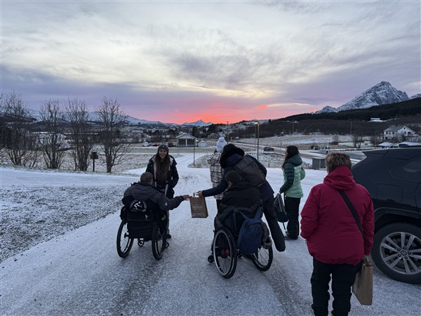 mensen in een rolstoel en te voet geven lunchpakketten aan elkaar bij zonsopgang tussen de bergen
