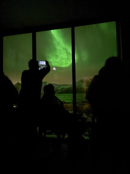 schaduwen van mensen waarvan 1 in een rolstoel bij een groot raam die foto's maken van noorderlicht