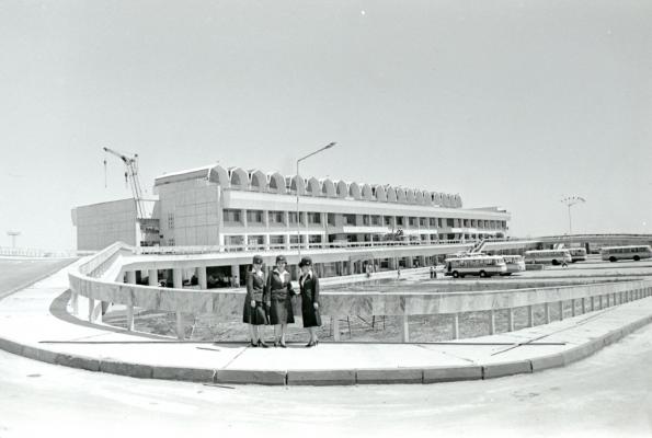 Stewardessen poseren voor een luchthaven in aanbouw op een talud met reisbussen op de achtergrond