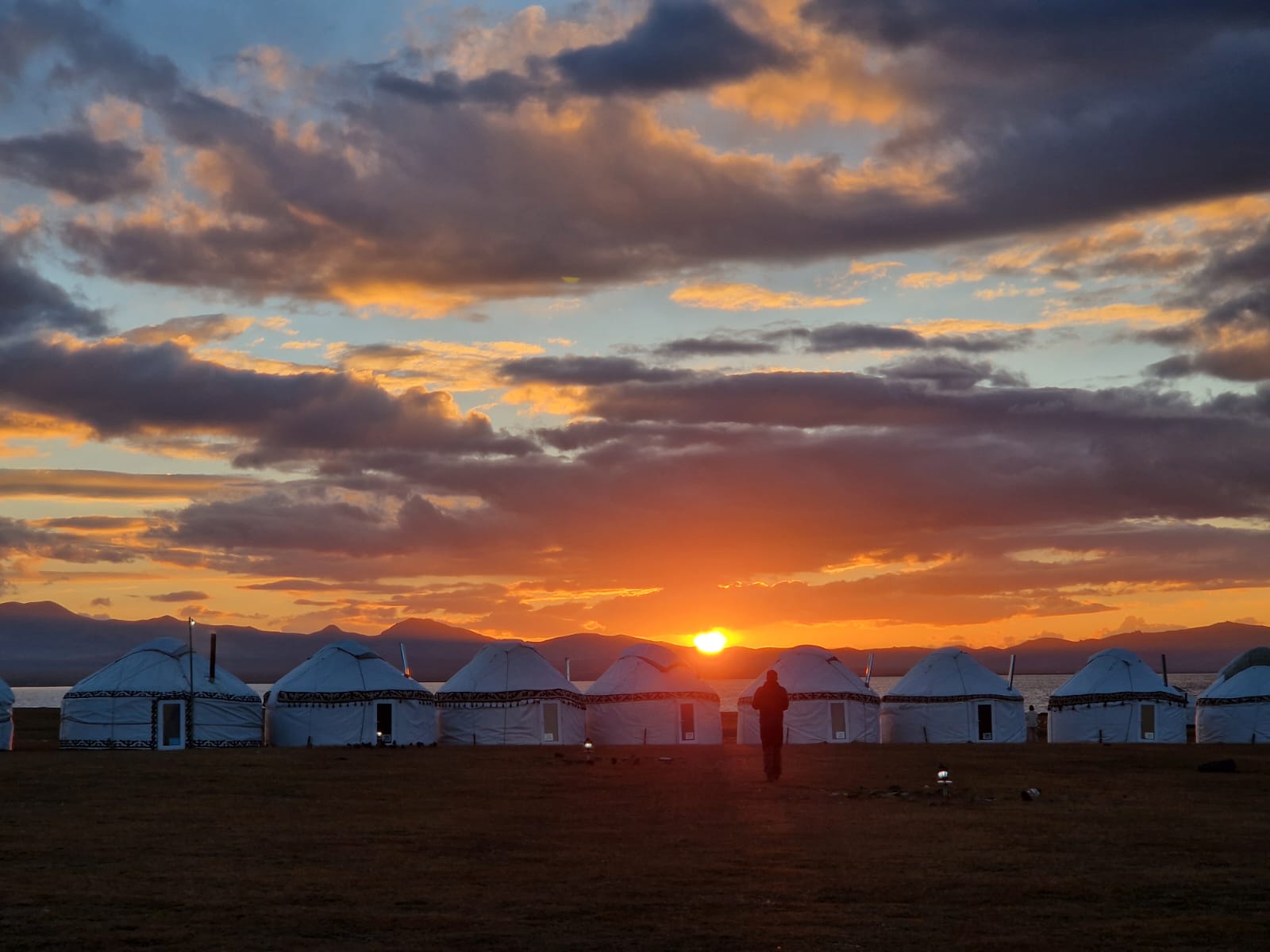 Een rij met yurts op een grasvlakte met ondergaande zon boven de bergen