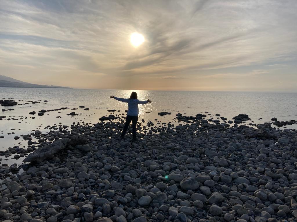 Een vrouw bewonderd de natuur uitkijkend over een groot meer en staande op een strand van keien