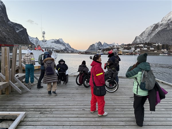 Mensen, sommige in een rolstoel, op een steiger in een haven op de Lofoten in de winter