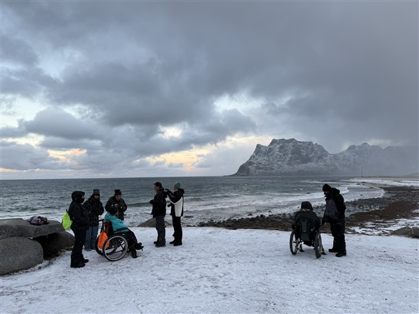Mensen waarvan 2 in een rolstoel op een besneeuwd strand op de Lofoten
