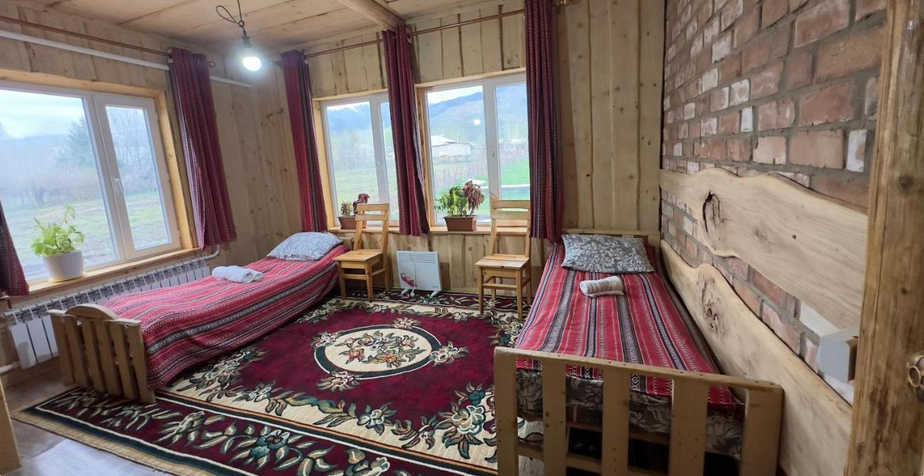 Kamer met twee bedden op een tapijt en stenen muren met houtwerk en veel licht door de ramen met uitzicht op bergen