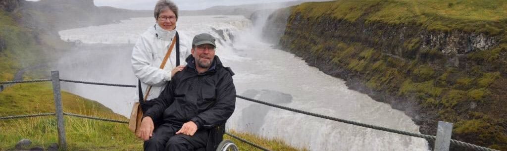 Twee mensen waarvan 1 in een rolstoel bij een grote waterval op IJsland