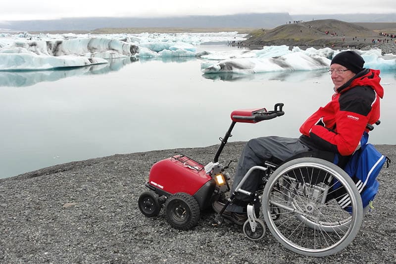 Man in een rolstoel kijkt uit over een gletsjermeer met ijsbergen in IJsland.
