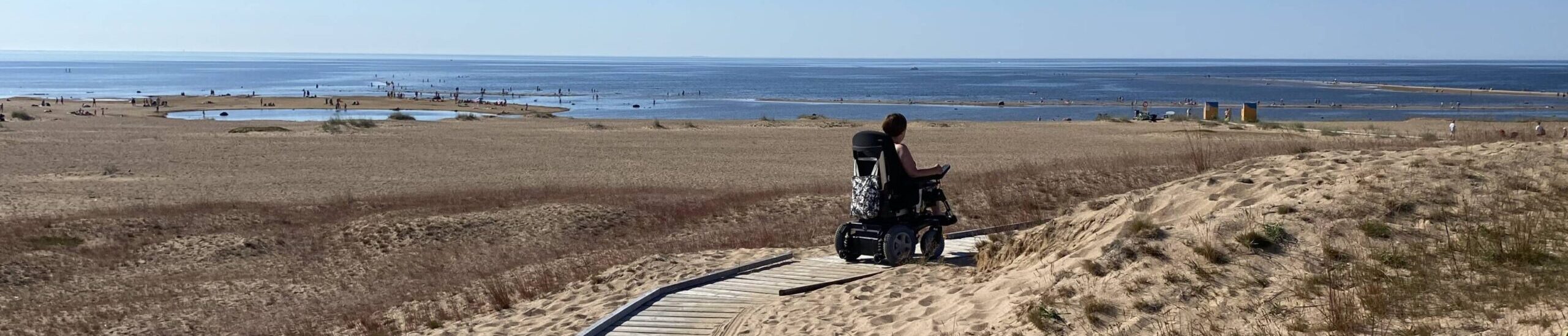Een vrouw rijdt in een rolstoel naar het strand over een houten pad