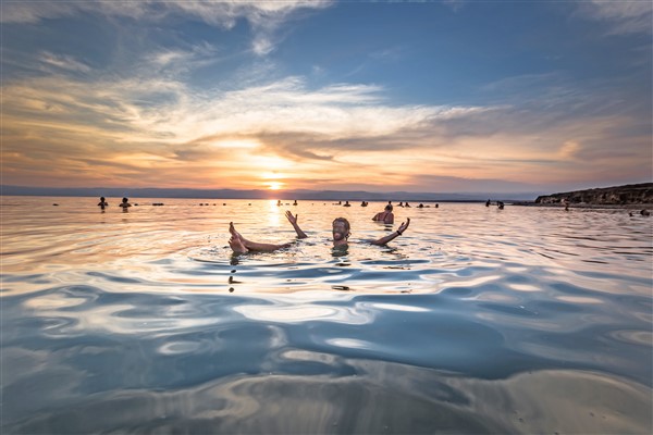 Mensen driven in het water van de Dode Zee tijdens zonsondergang
