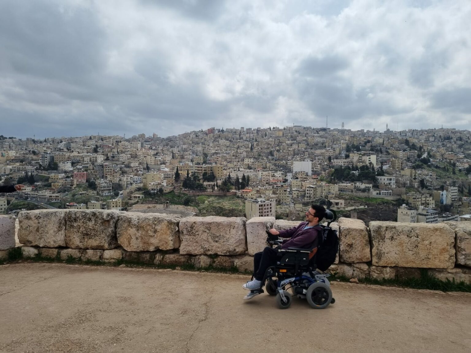 Een man in een rolstoel rijdt over de citadel van Amman in Jordanië met op de achtergrond de stad