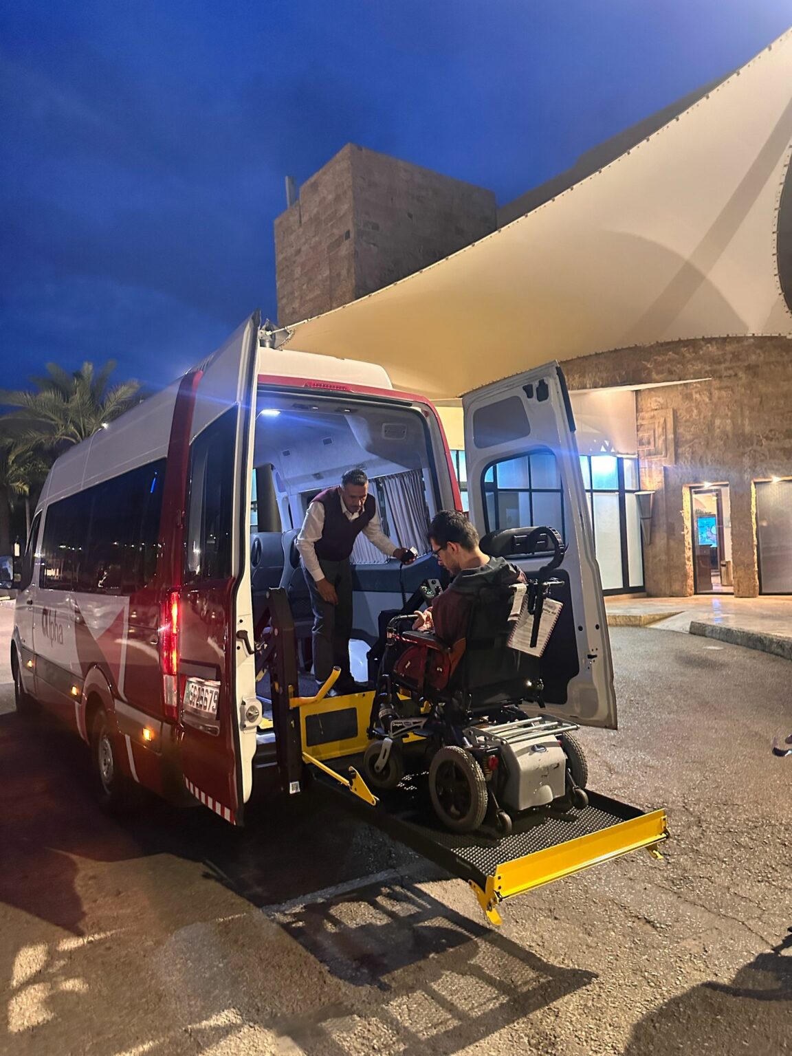 Een rolstoelgebruiker wordt via een lift in een toegankelijk busje gereden bij een hotel