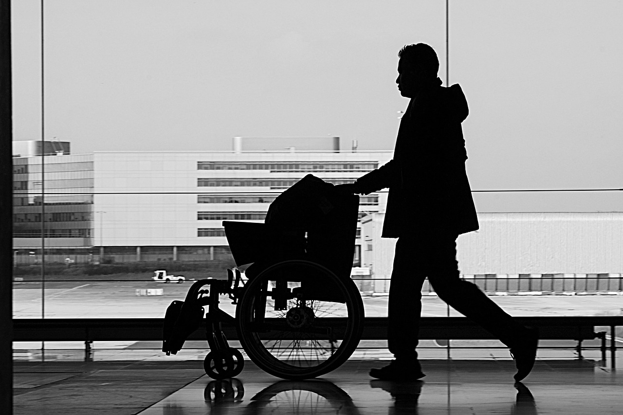 Silhouet van een man die een lege rolstoel duwt op een luchthaven