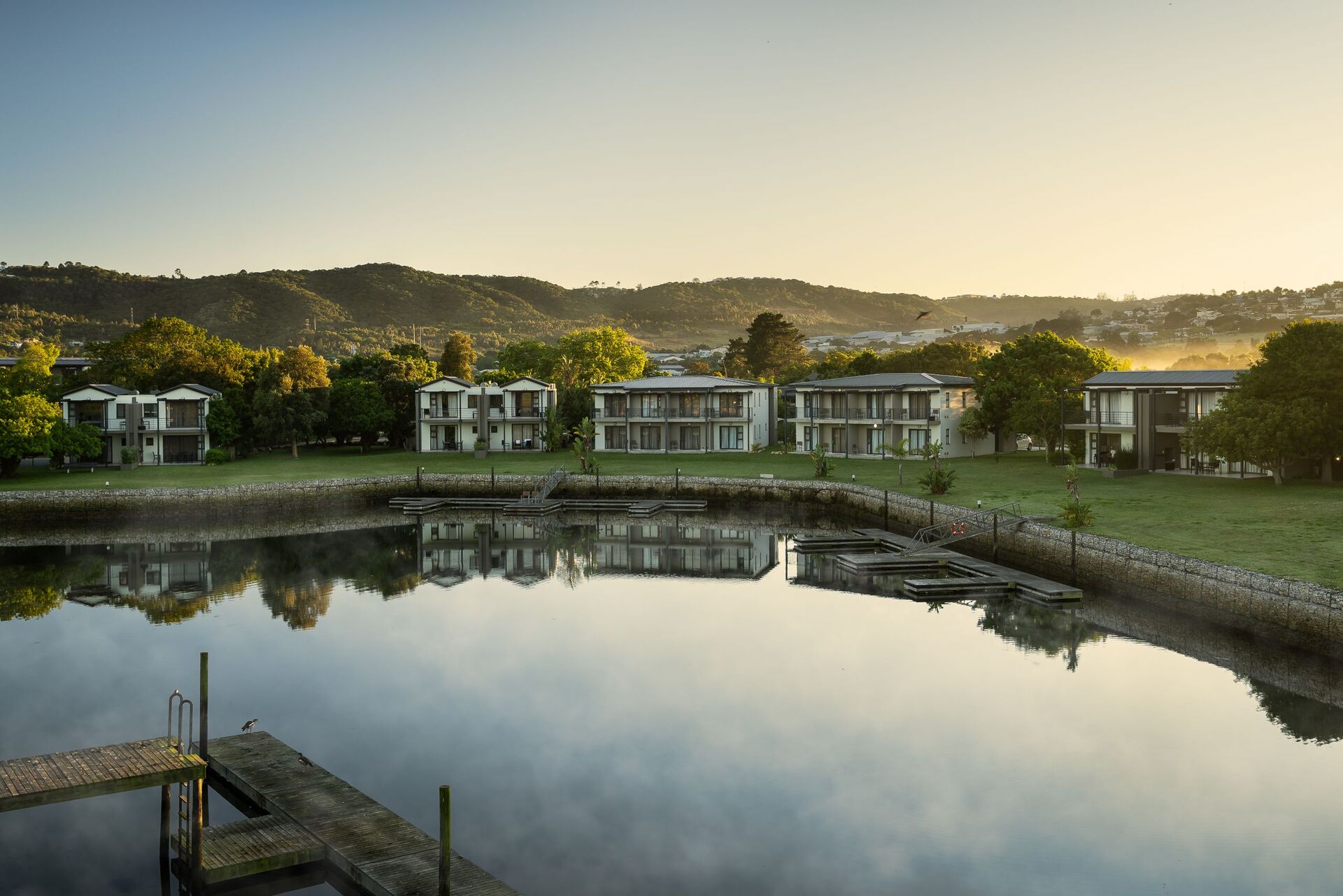 Een aantal hotel appartementen aan de oever van een rivier met bos en in de achtergrond bergen